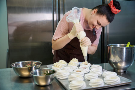 Focused woman confectioner decorating set of merengue nests with custard