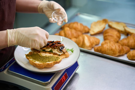 Close-up view baker adding sliced olives on half of croissantの写真素材