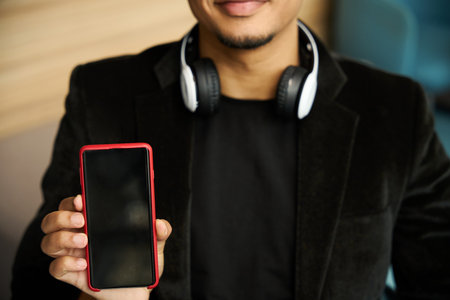 Happy guy wearing headphones on neck showing phone screenの写真素材
