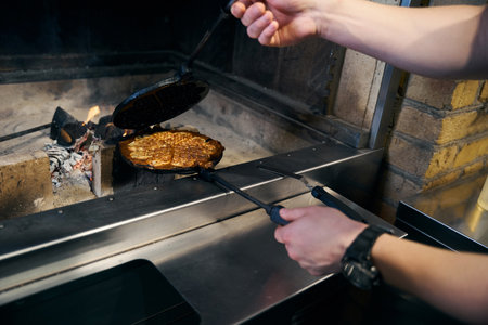 Partial chef frying pancake in pancake maker in burning fire place in restaurantの写真素材