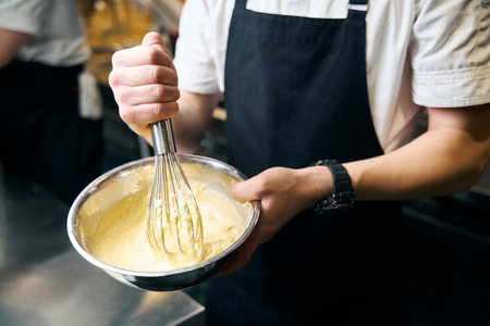 Cropped male chef mixing dough with whisk in bowl for cooking dish in restaurantの写真素材
