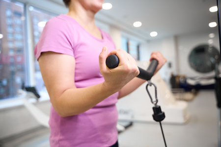 Focus on foreground of woman doing sport exercise for biceps in blurred gym