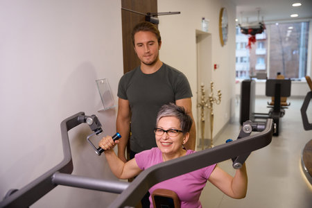 Male trainer looking at smiling mature caucasian woman doing exercise for back