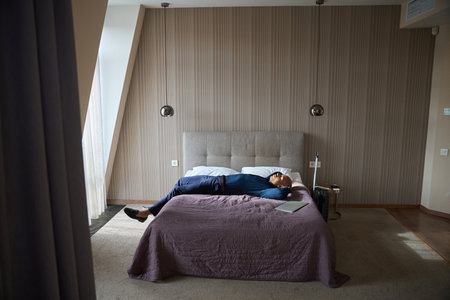 Side view of tired african american male entrepreneur lying and resting on bed