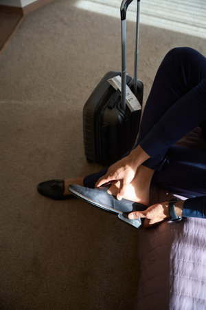 Top view of cropped african american male entrepreneur putting on shoe on bed