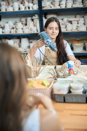 Woman drying clay plate with special dryer in workshop