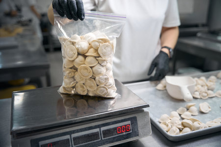 Workshop worker weighs a package of frozen dumplings on scaleの写真素材