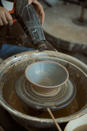 Expert potter drying earthenware bowl on pottery wheel using dryer tool