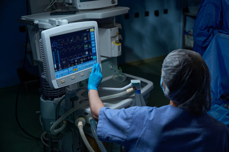 Young female assistant in gloves, mask and uniform pointing at display of medical equipment