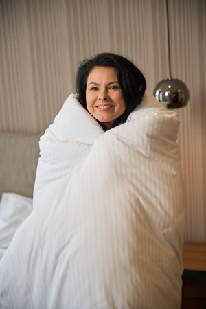 Happy woman wraps herself in a fluffy blanketの写真素材