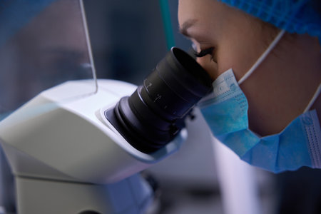Female embryologist closely observing through a microscope