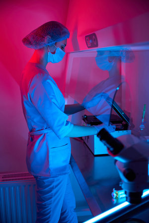 Embryologist operating lab equipment in a colored light environmentの写真素材