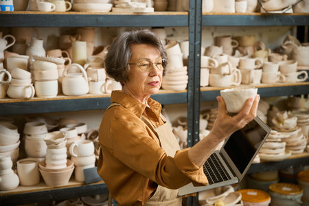 Lady holds clay bowl in one hand and laptop in therの写真素材