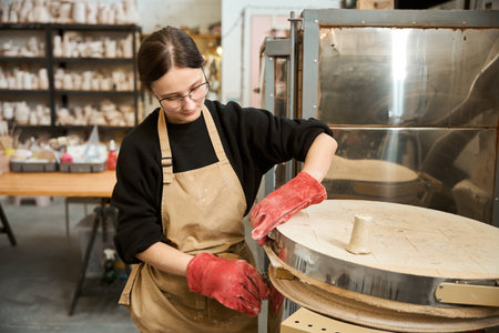 Craftswoman in red work gloves works in a ceramics studio