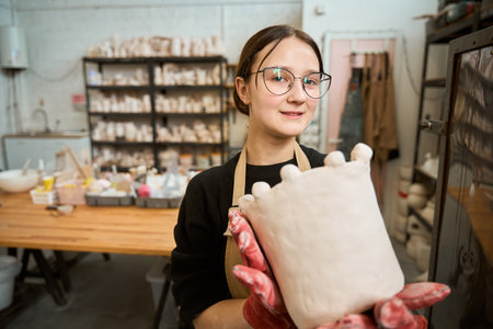 Young woman in protective gloves holding clay productの写真素材