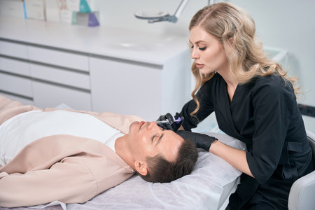 High-qualified cosmetician making filler injections into male client lipsの写真素材