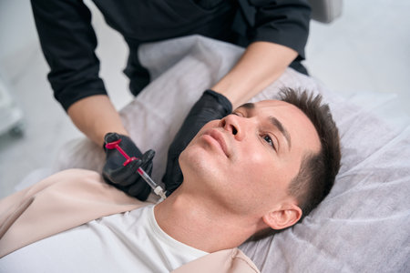 Focused state-licensed beautician making injections of filler into male neckの写真素材