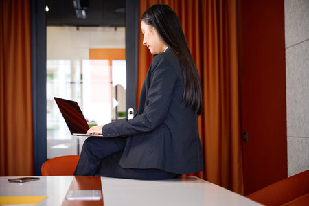 Smiling woman sat on edge of conference table with laptopの写真素材