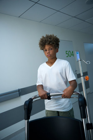 Young boy pushes medical chair through brightly lit hospital hallwayの写真素材