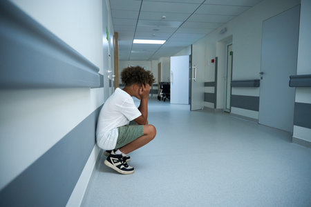 Young patient crouches down in a hospital corridorの写真素材
