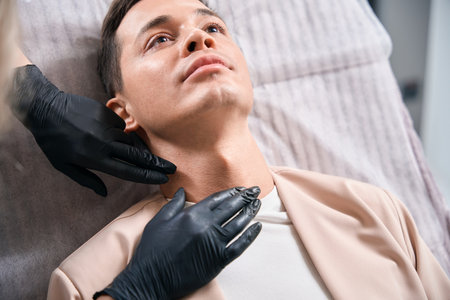 Woman cosmetologist in rubber gloves examining male client neckの写真素材
