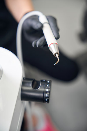 Female dentist adjusting speed of scaler before starting patient teeth treatment