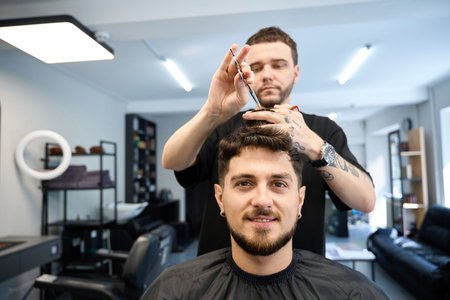 Stylist doing modern haircut to client in barber shopの写真素材