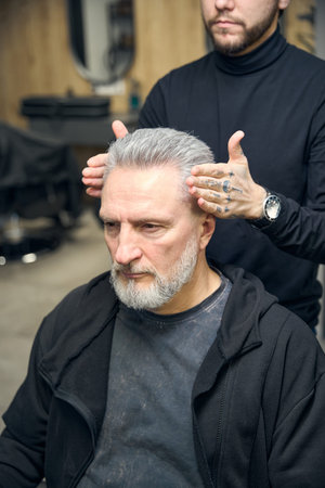 Stylish hairdresser making final touches for adult man