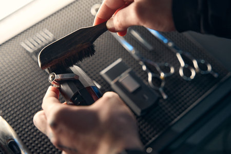 Cropped view of hairdresser cleaning hair clipper in barber shop