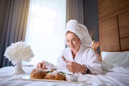 Young woman enjoying breakfast in bed with croissants and fruitの写真素材