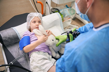 Young girl with stuffed rabbit and adult in medical attire indoorの写真素材