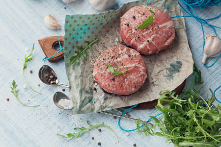 Organic raw ground beef wrapped in strips of bacon. Round patties for making homemade burger on wooden cutting board with herbs. Top view with space for text.の写真素材