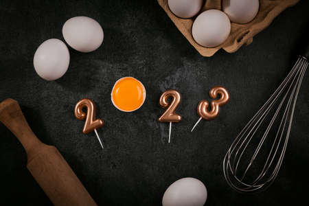 Creative Happy New Year 2023 greeting card for home baker. Numbers made out of numeric candles with egg yolk, Christmas baking concept, top viewの写真素材