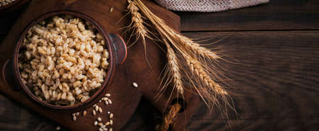 Bowl of cooked peeled barley grains porridge with ears of wheat on dark wooden background. Cooking Healthy and diet food concept.の写真素材