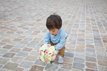 Cute little boy holding a bouquet of flowers. mother's day. International Women's Day. Portrait of a little eastern handsome baby boy playing outdoor with a flowersの写真素材