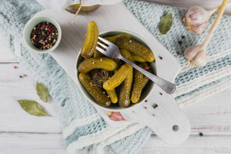 Gherkins, pickled cucumber on a fork, bowl of marinated vegetables on white wooden background. Clean eating, vegetarian food concept. top view, close upの写真素材