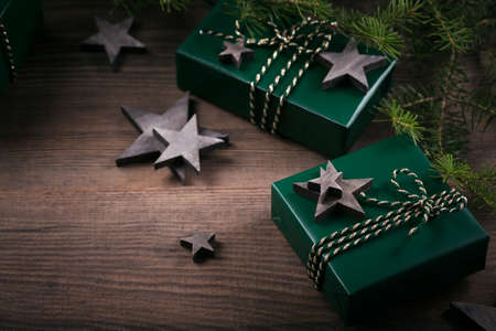 Christmas frame with green gift boxes, wooden star decorations, fir cones and spruce branches on dark wooden background. Holiday background in natural earth colours.の写真素材