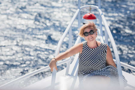 Woman relaxing on the nose of the yacht at a sunny summer day at sea and enjoying at vacation and luxury travelの写真素材