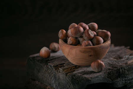 Pile of hazelnuts filbert in a wooden bowl on a dark wooden background. Fresh nuts in their shells.の写真素材