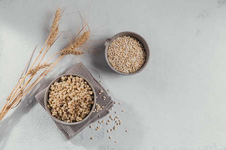 Organic uncooked dried barley cereal grain in a bowl and pearl barley porridge with ears of wheat on...