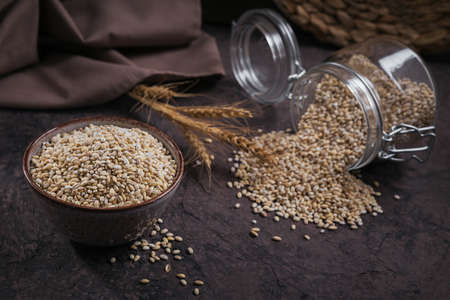 Bowl of dry raw broken pearl barley cereal grain on dark background. Cooking pearl barley porridge concept.の写真素材