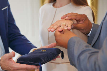 Mixed race couple holding hands and exchanging wedding ringsの写真素材