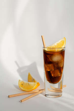 Glass of cola with ice, lemon and straw on a white background