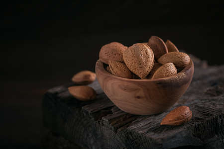 Pile of Almond nuts in a bowl on a dark wooden background. Fresh nuts in their shells.