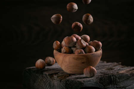 Pile of hazelnuts filbert in a wooden bowl on a dark wooden backgroundの写真素材