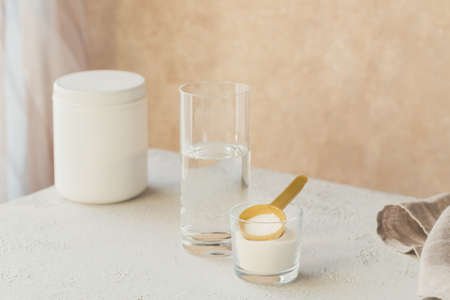 Collagen powder in bowl, glass of water and measure spoon on white wooden background. Extra protein intake. Natural beauty and health supplement concept.の写真素材