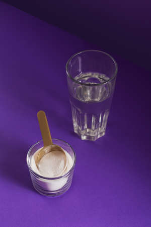 Glass with collagen dissolved in water and collagen protein powder on purple table. Healthy lifestyle concept.の写真素材