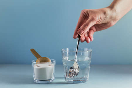 Glass with collagen dissolved in water and collagen protein powder on light blue background. Woman's...