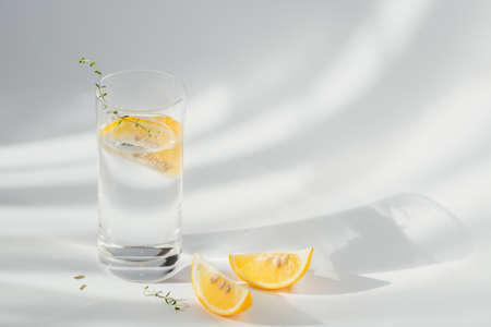 Glass of clean mineral sparkling water with ice and lemon on a white background with sunshine. Light with hard shadows and glare from the glass. Breakfast, fresh morning drinkの写真素材