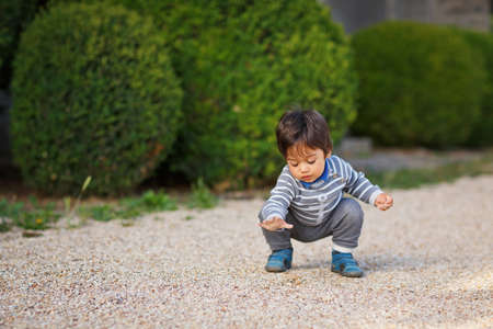 Portrait of a little eastern handsome baby boy playing with pebbles outdoor in the park. Arabian child fun on the street with pebbles.の写真素材